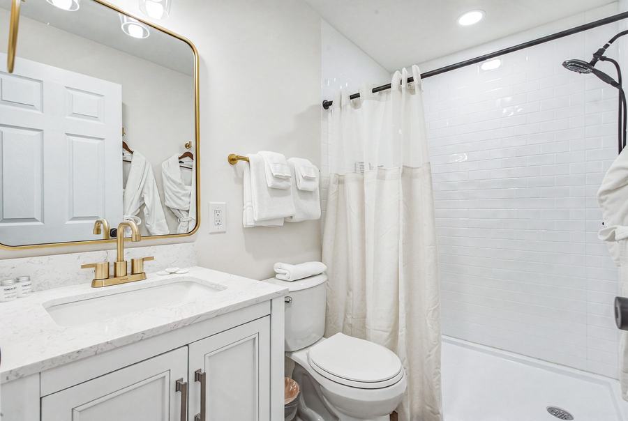 Bright private bathroom with white vanity, gold-tone fixtures, toilet, and shower