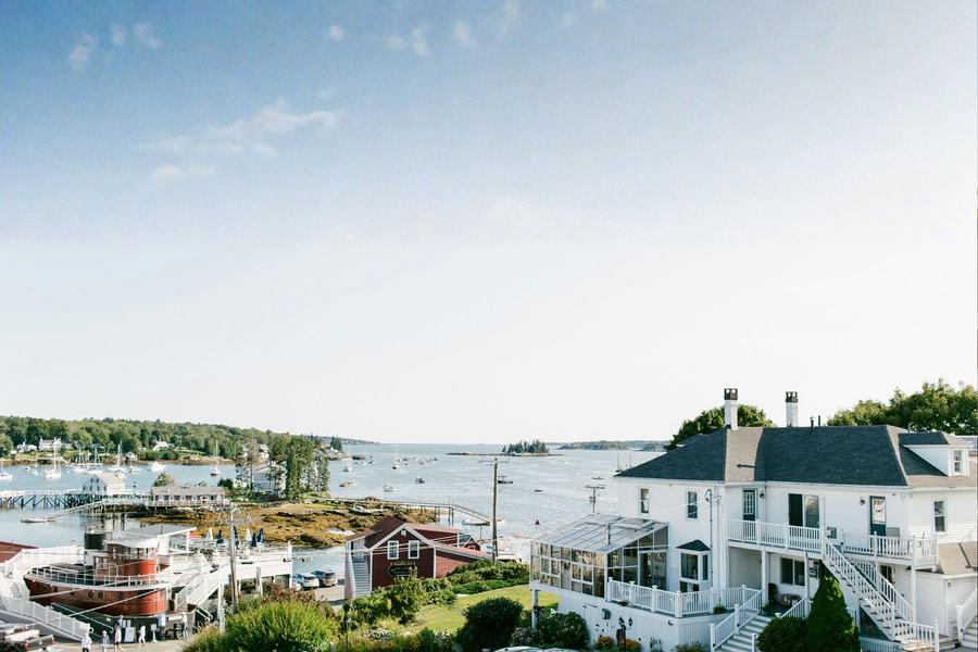 Scenic harbor with boats, waterfront homes, and ocean views under a blue sky.