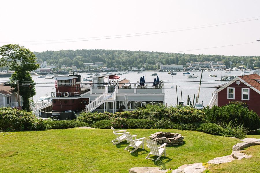Waterfront lawn with Adirondack chairs around a stone fire pit overlooking Boothbay Harbor.