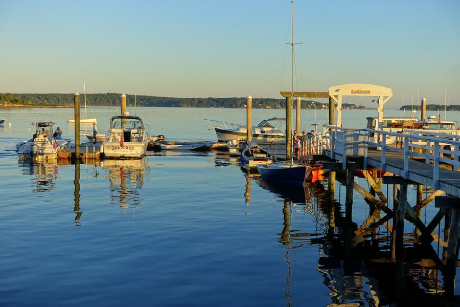 A quiet stretch of Boothbay Harbor waterfront at dusk with boats reflected in calm water