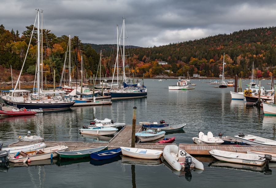 Autumn foliage in red and gold above the boats and white buildings of Boothbay Harbor, Maine